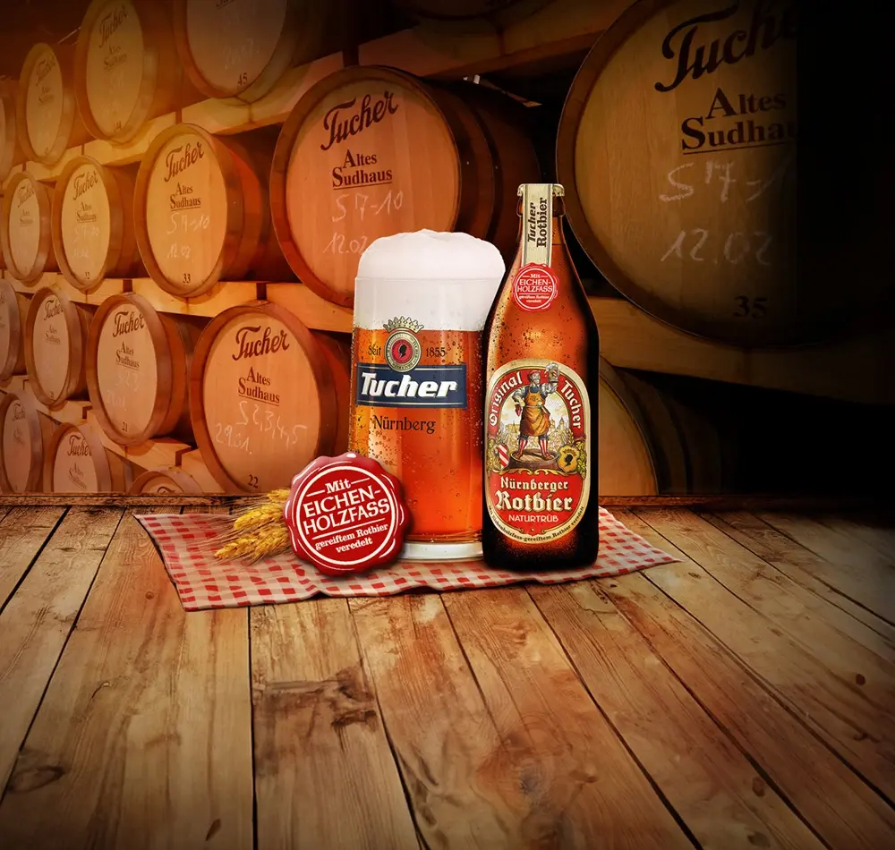 Ein Glas Bier und eine Flasche stehen vor Fässern auf einem Holztisch.