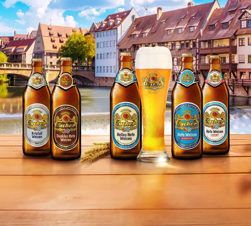 Fünf Bierflaschen und ein volles Glas stehen vor einer Flusskulisse mit Häusern.