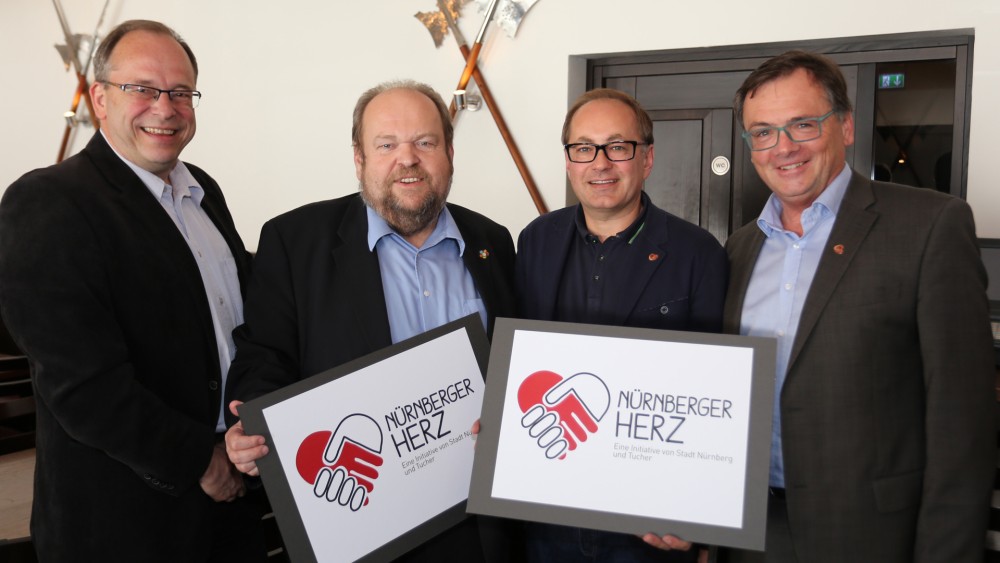 Vier Männer stehen nebeneinander und halten zwei Schilder mit einem Herzlogo.