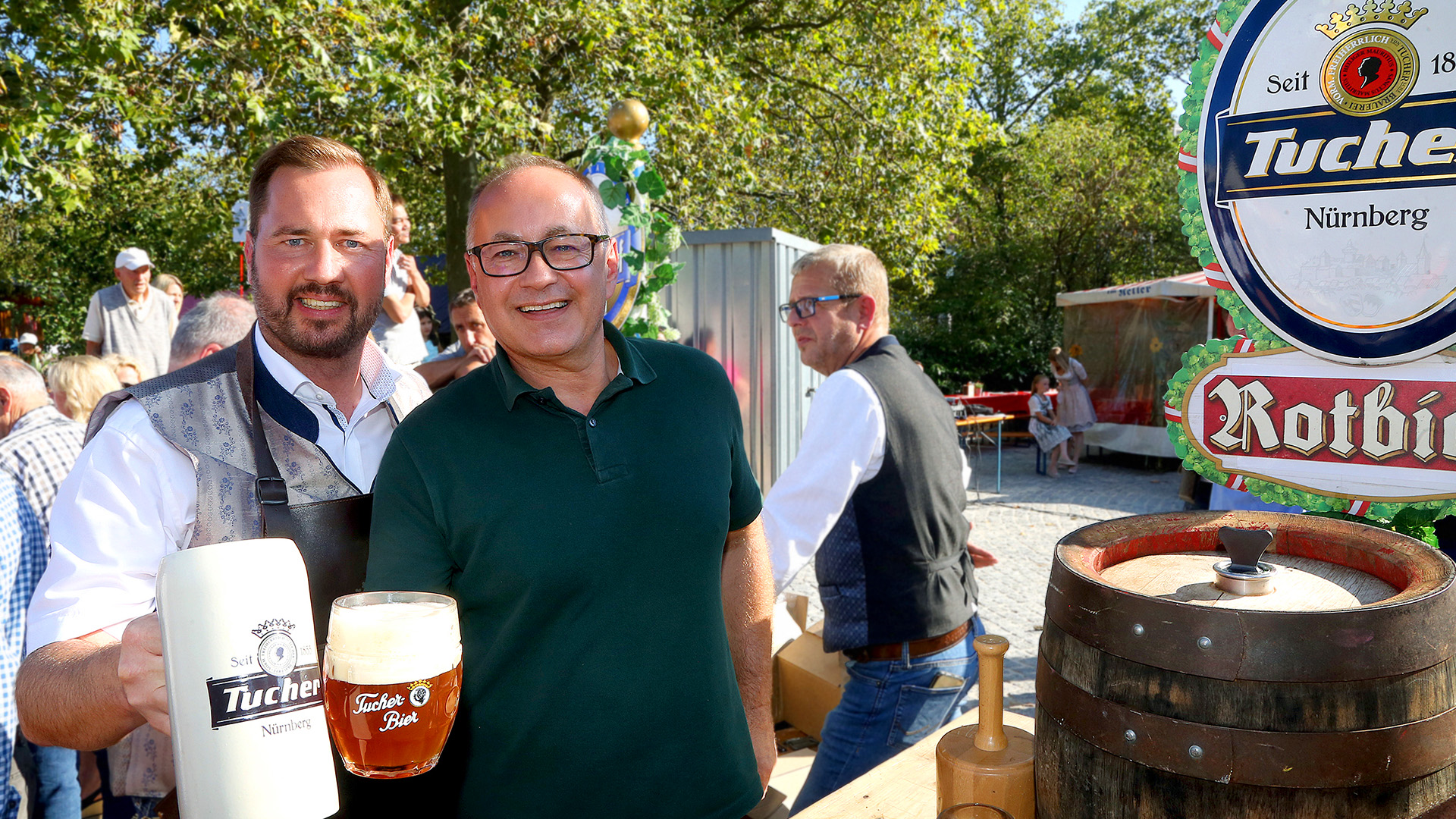 Zwei Männer lächeln und halten Getränke auf einem sonnigen Fest.