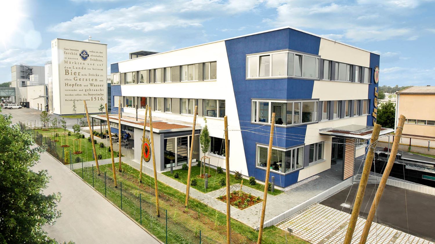 Ein modernes zweigeschossiges Gebäude mit blauen und weißen Fassaden steht neben einem Bierwerbungsturm.