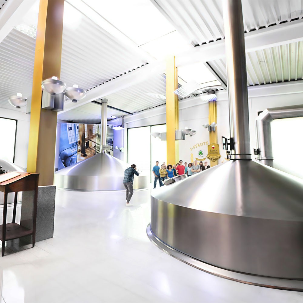 In einer Brauerei sind große Kessel zu sehen und Personen, die eine Führung erhalten.